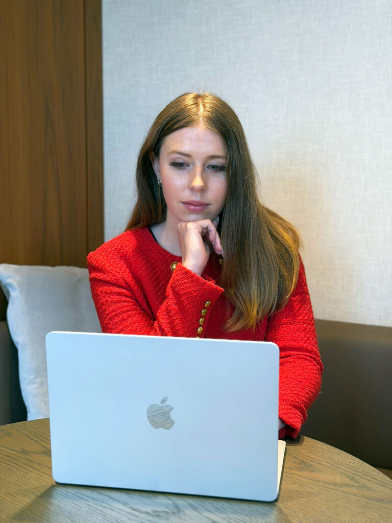 Grace Dunn focused on her laptop at a table in a red jacket — reviewing a personalized SAT and ACT coaching plan for a student