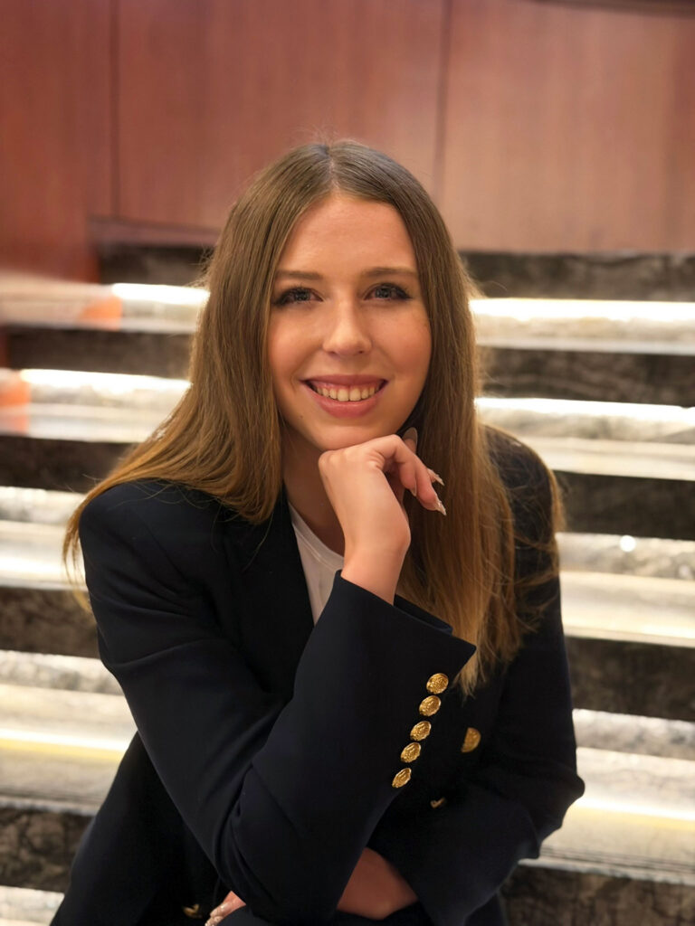 Grace Dunn seated on marble stairs in a navy blazer with a warm smile — founder of Crownridge Coaching and elite SAT tutor